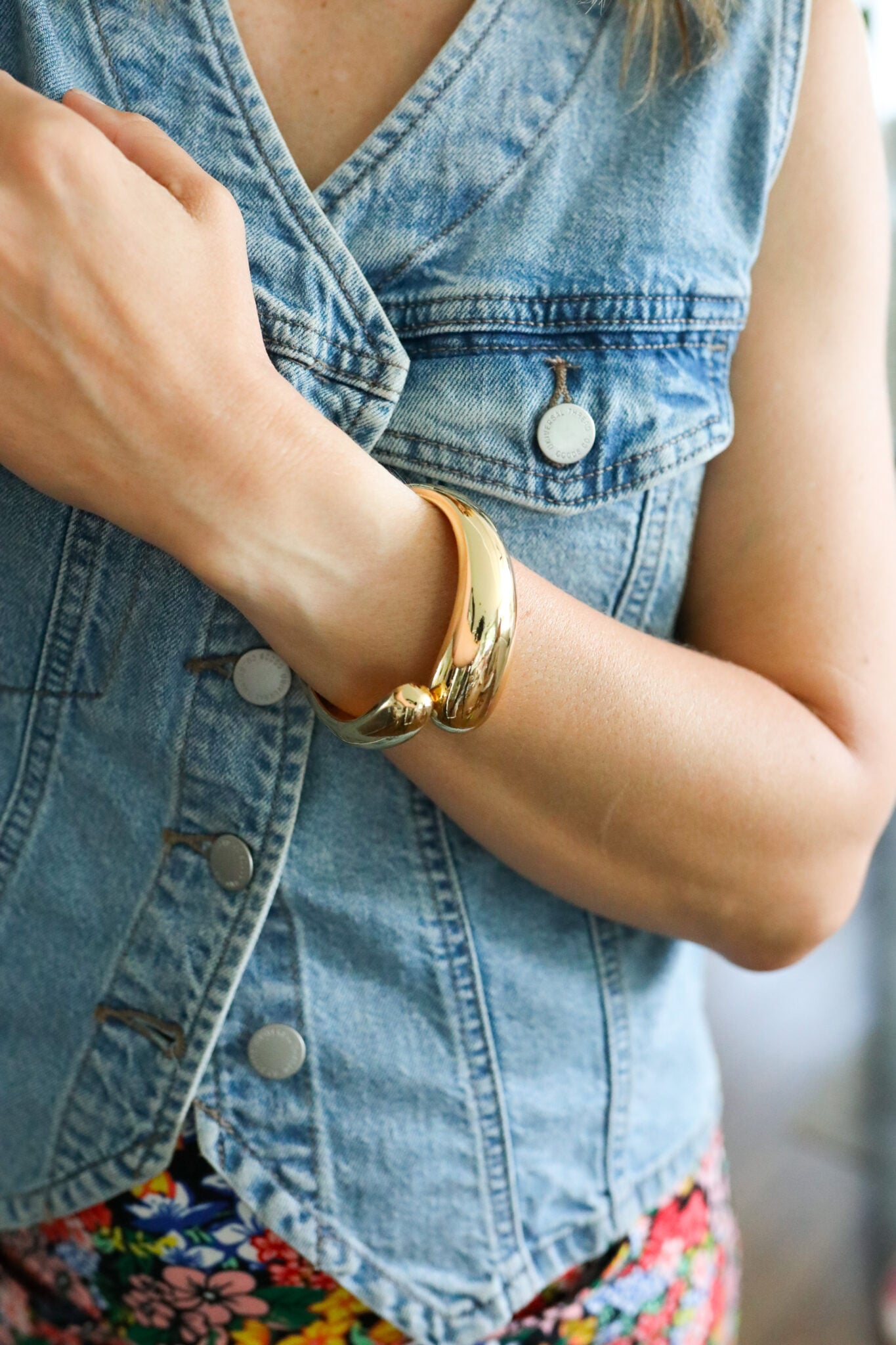 Close-up of a chunky twisted gold bangle styled on a wrist denim vest