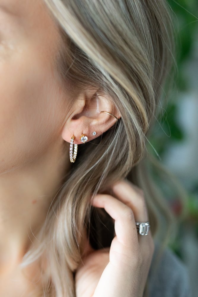 Close-up of three earrings styled on one ear ā small hoops and dainty studs layered together