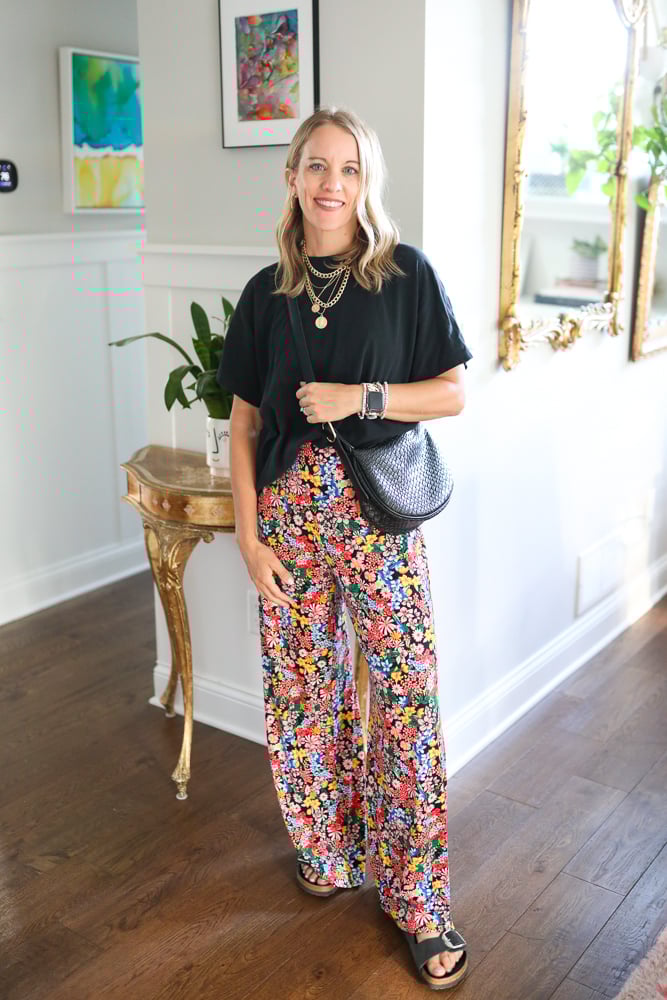 Jen styled in an oversized polished tee, floral pants, black textured bag, gold necklace, and black Birkenstock sandals for a laid-back yet chic look