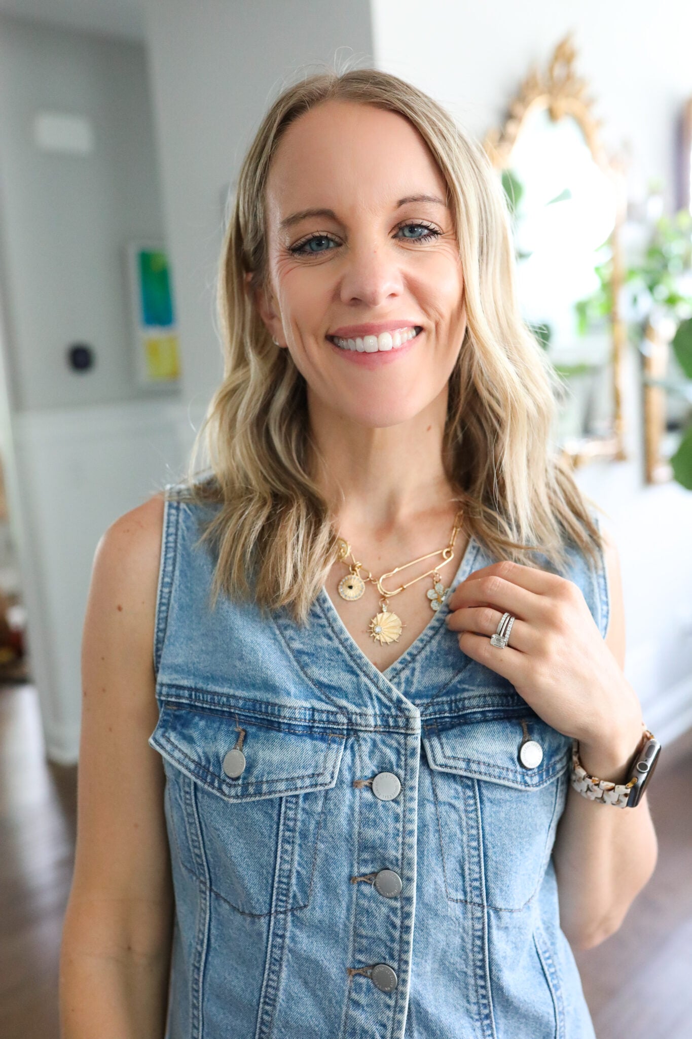 Image shows a layered gold charm necklace with paperclip chain and dainty evil eye, sun, and flower pendants.