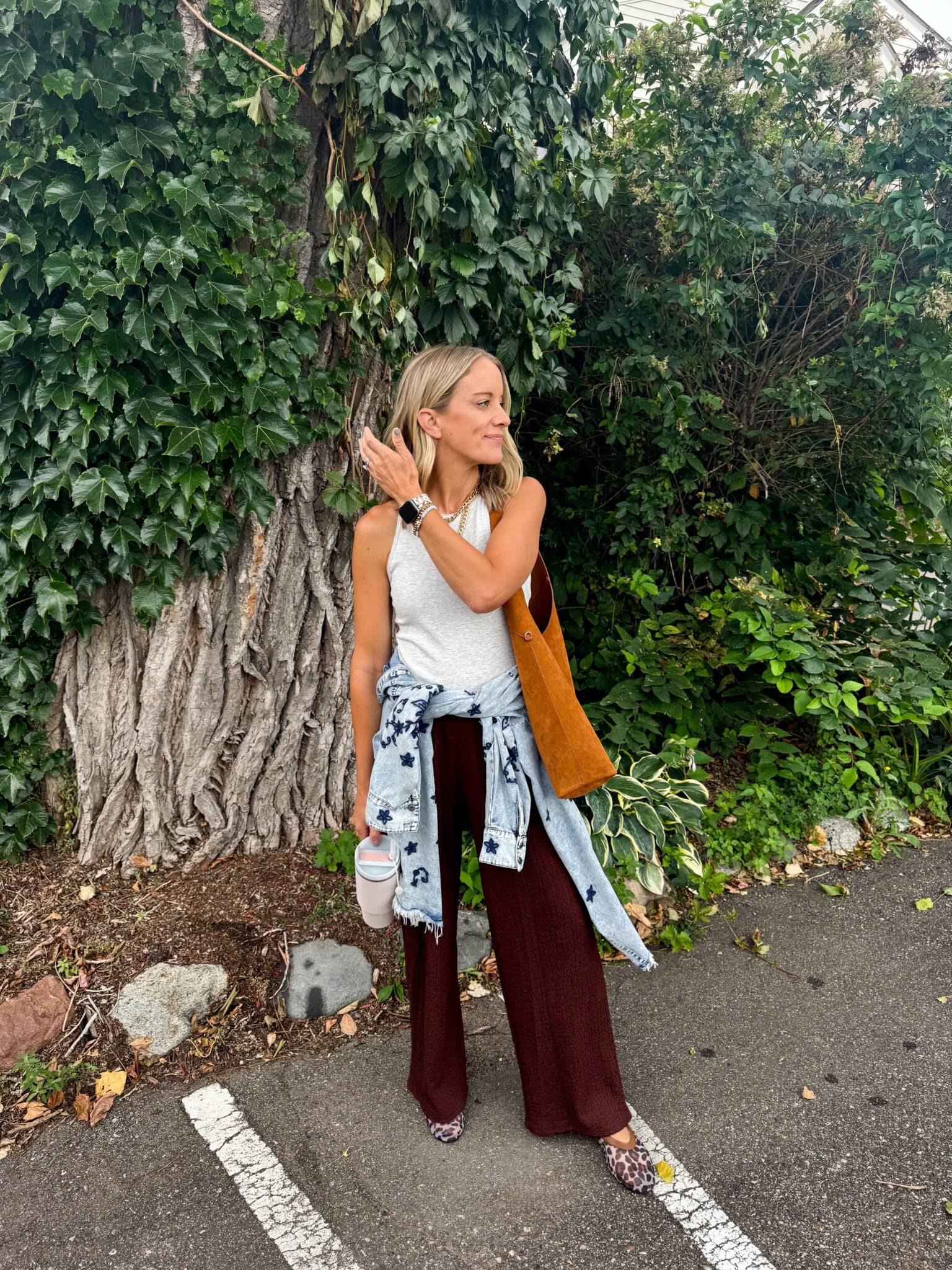 Jen Paisley of Paisley and Sparrow in a casual fall outfit with chocolate brown wide-leg pants from Target, light grey Vuori tank top, suede brown tote bag, leopard flats, and a denim jacket tied at the waist.