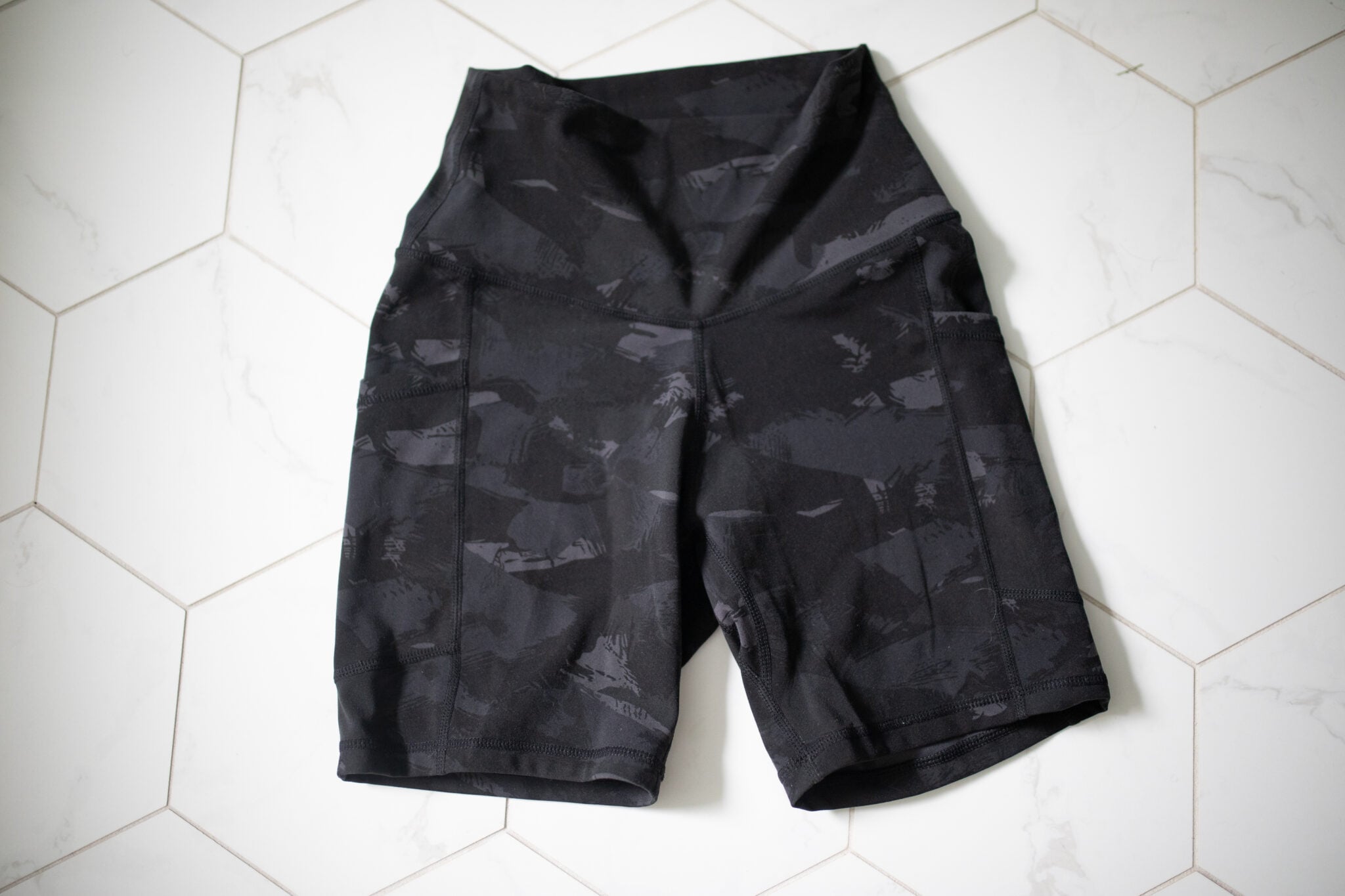 Flat lay of Colorfulkoala high-waisted biker shorts in a black camo print. Displayed on a white tile floor to show texture and detail.