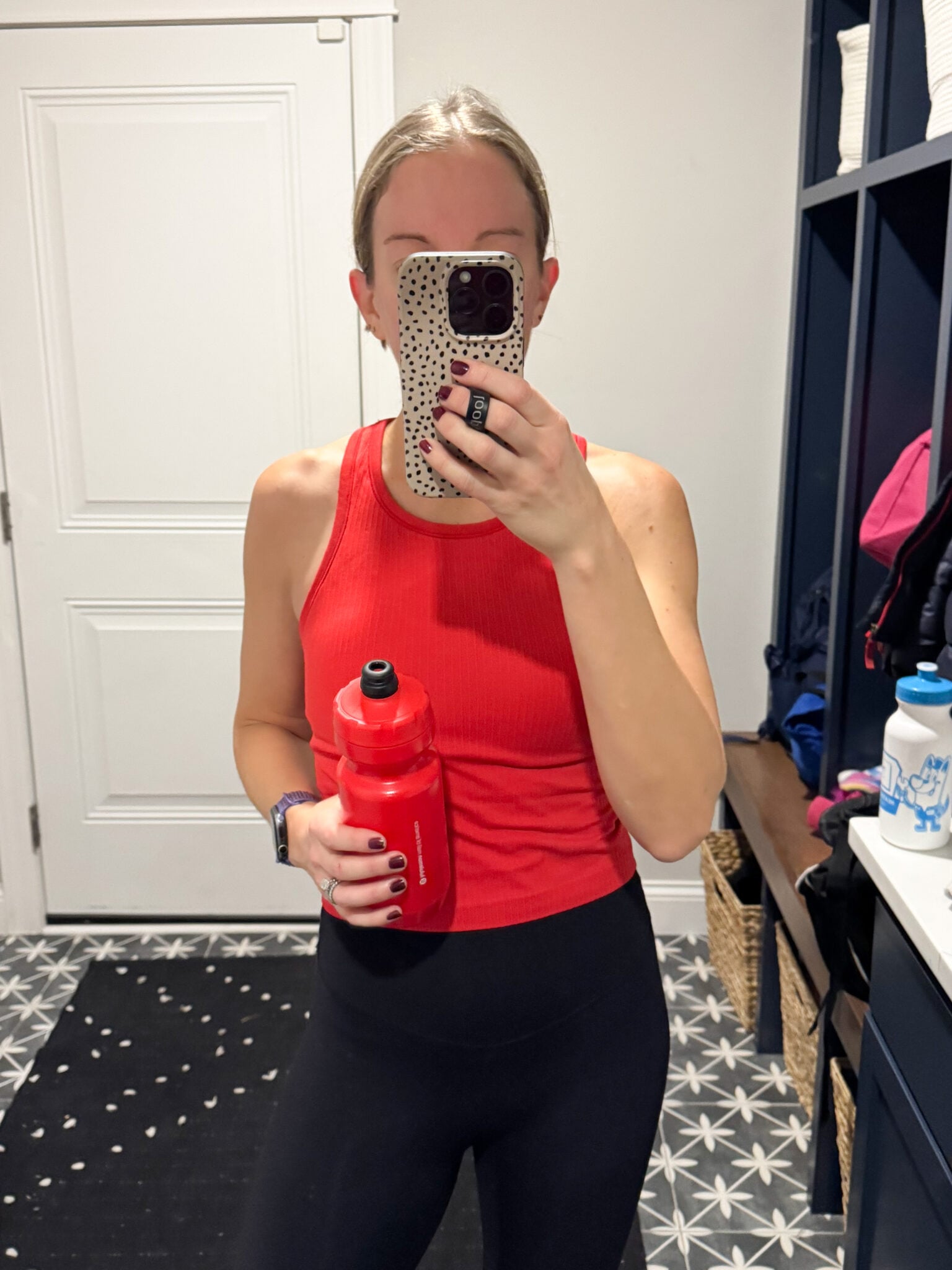 Mirror selfie of Jen in a red CRZ Yoga ribbed tank top and high-rise black Sunzel leggings. Holding a red water bottle post-workout in a locker room setting.