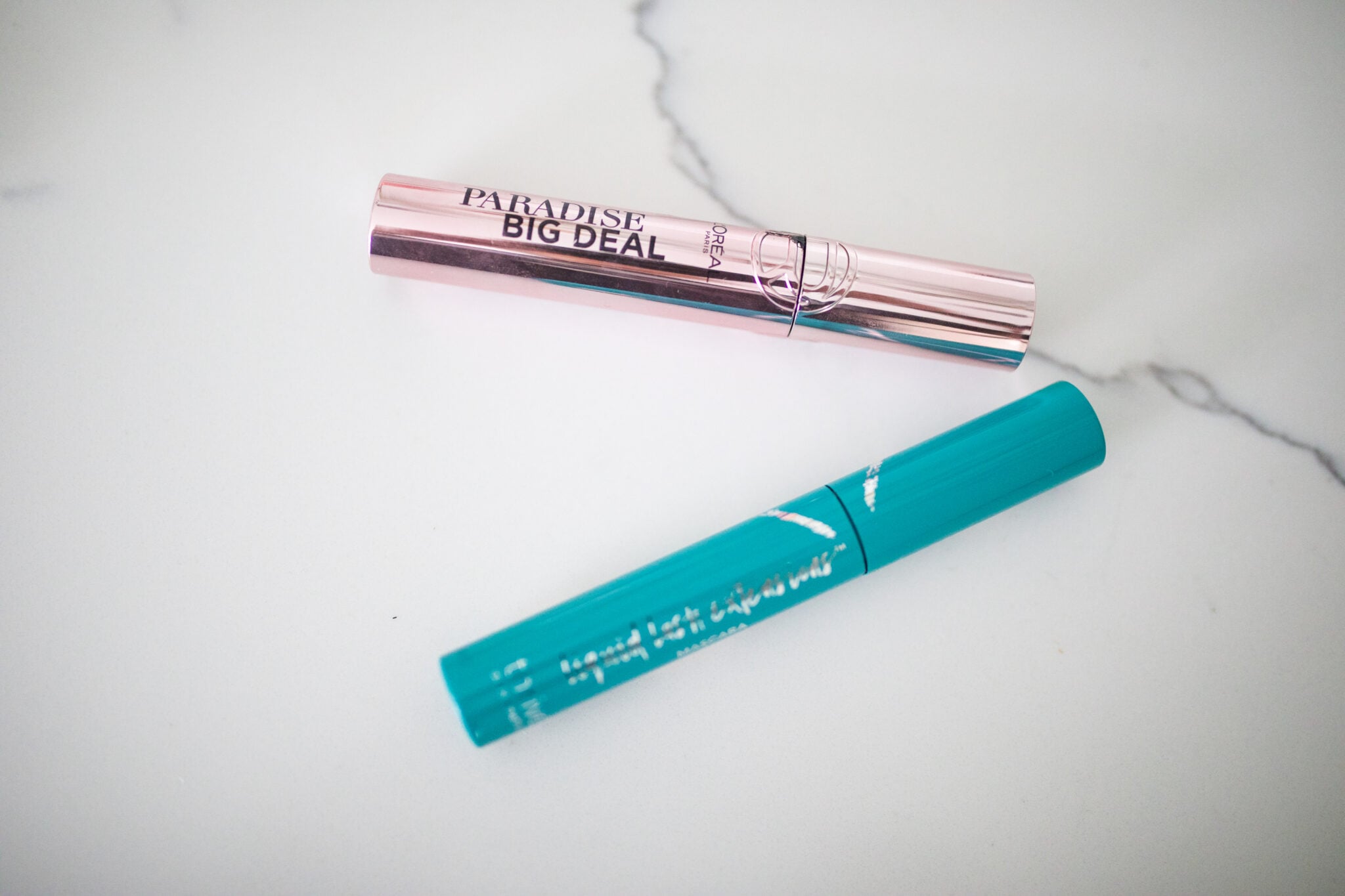 LāOreal Paradise Big Deal mascara in rose gold tube with teal Thrive Cosmetics Liquid Lash Extensions mascara tube on a white background.