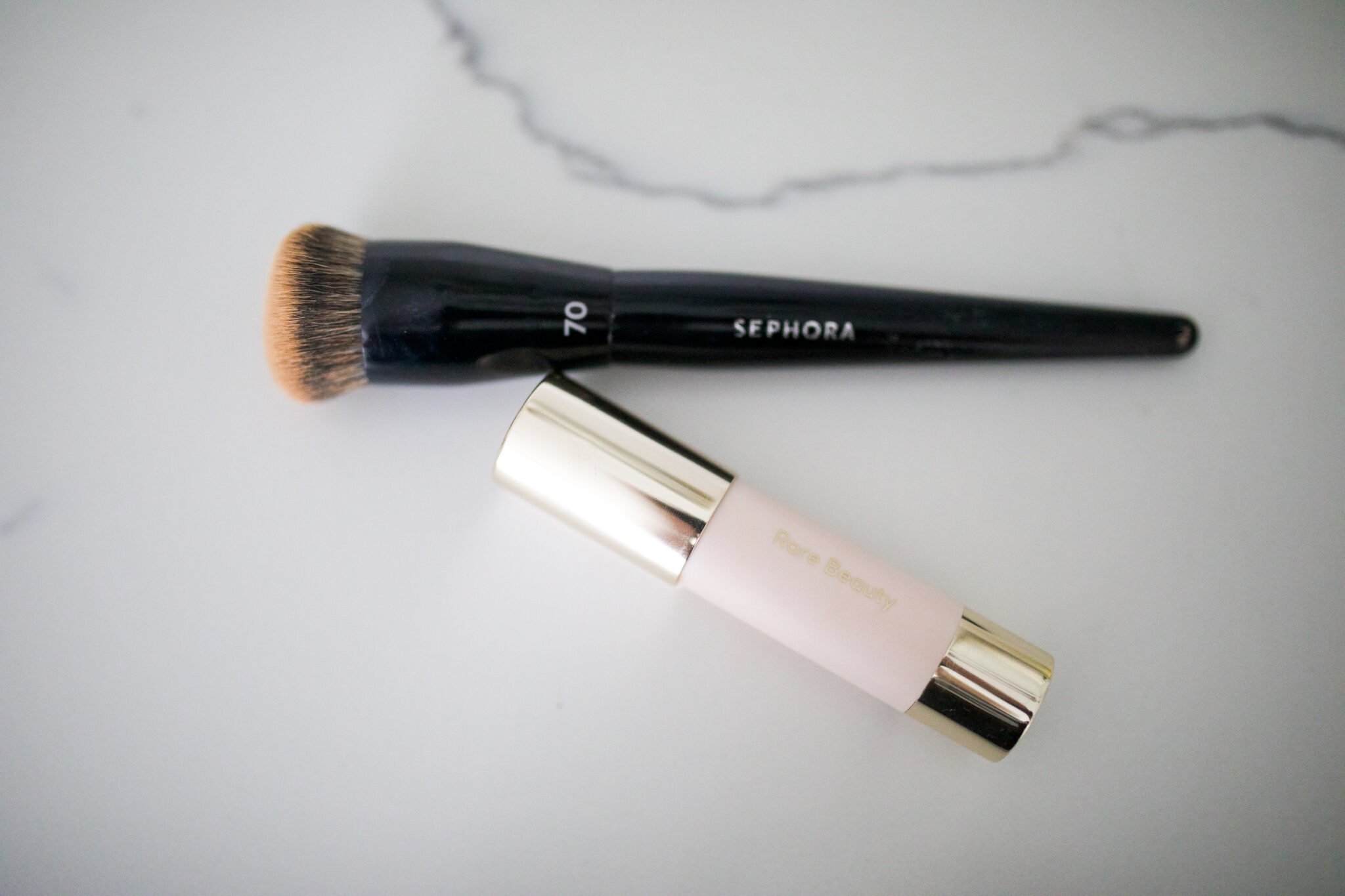 Rare Beauty concealer stick with Sephora 70 foundation brush on a white background.