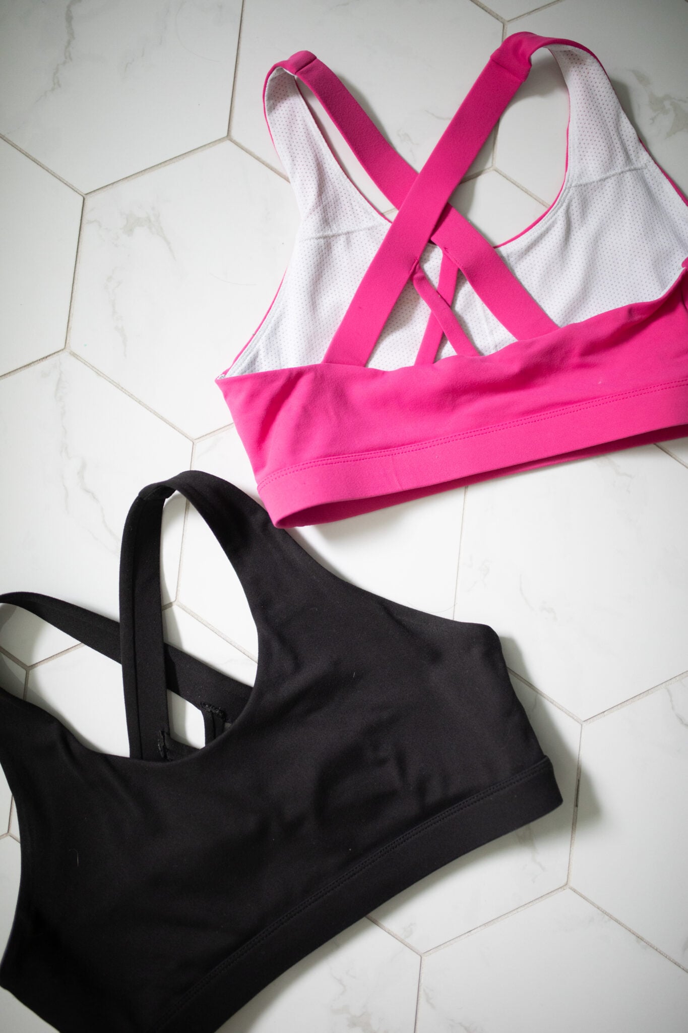 Flat lay of two sets of Baeleaf athletic wear, including magenta and navy sports bras with matching biker shorts. Displayed on a white hex tile floor to show color and fit options.