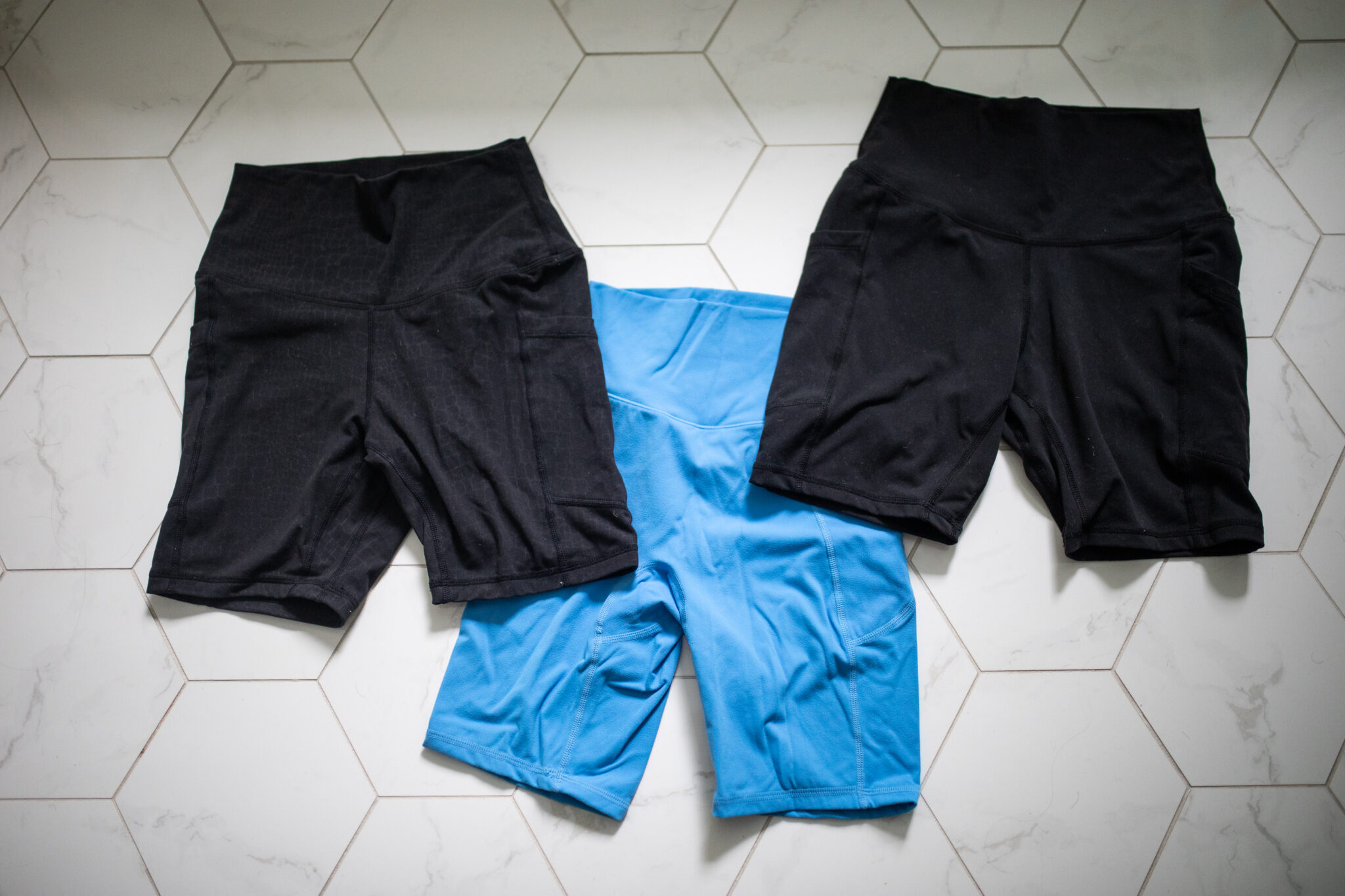 Flat lay of Colorfulkoala high-waisted biker shorts in a black camo print. Displayed on a white tile floor to show texture and detail.