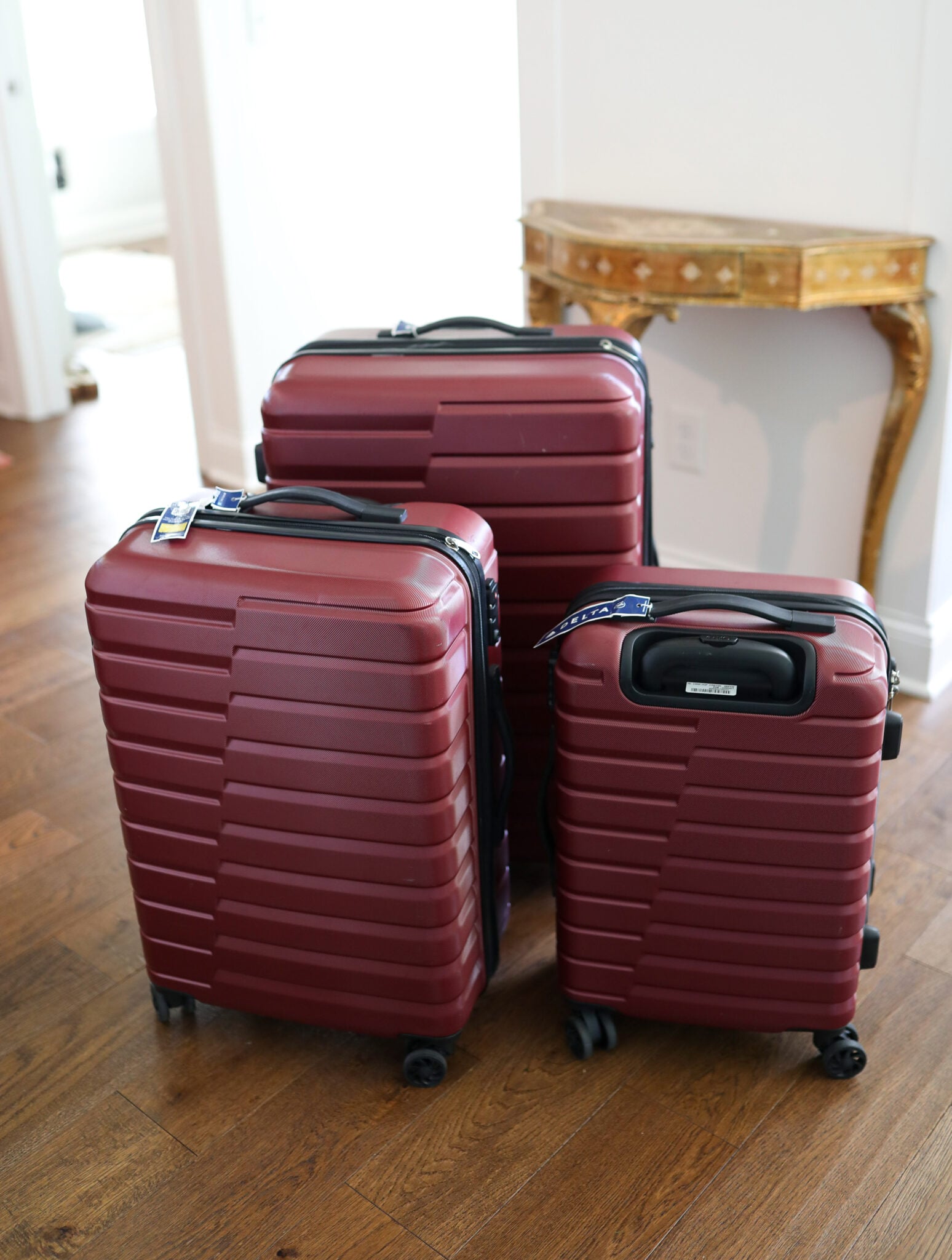 Three piece maroon hard shell luggage set with spinner wheels on a hardwood floor