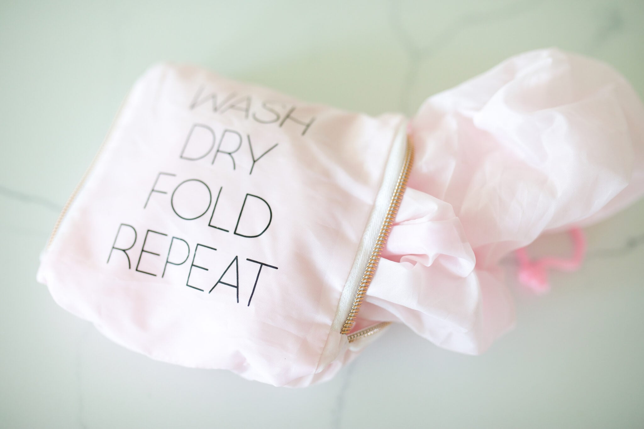 Pink travel laundry bag with zipper and printed words wash dry fold repeat