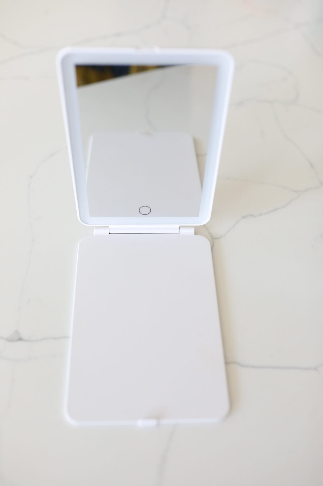 White rechargeable LED light travel mirror folded open on a counter