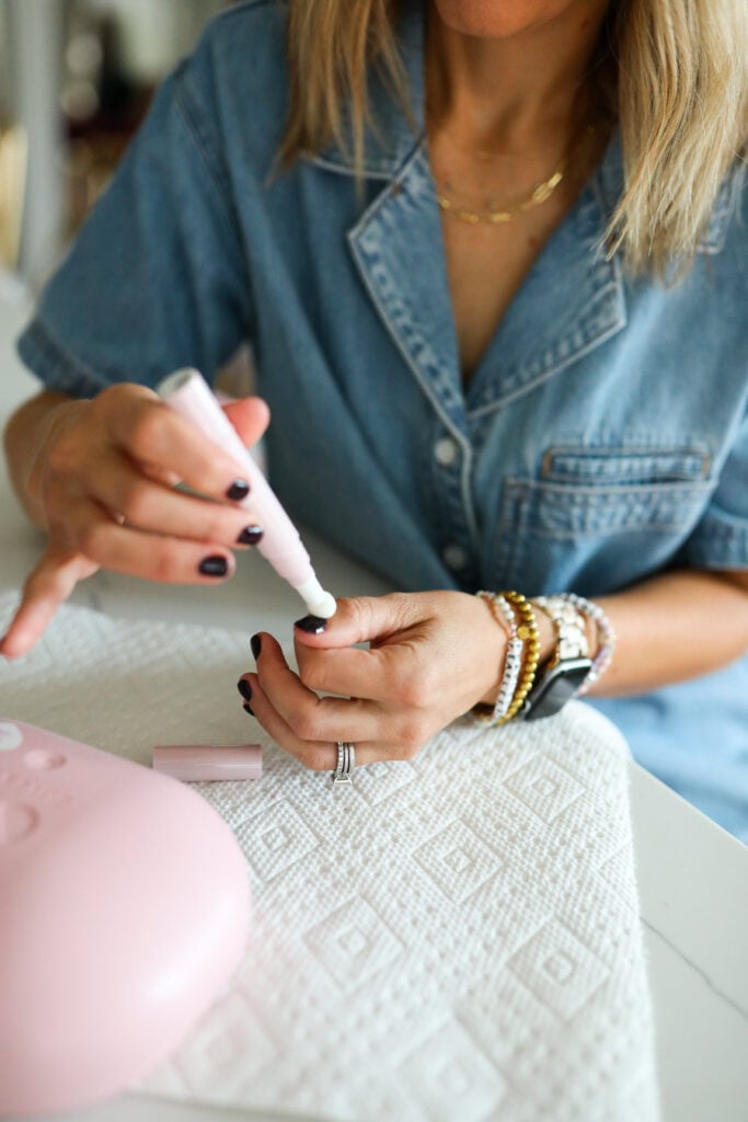 A woman putting cuticle serum on her nails.