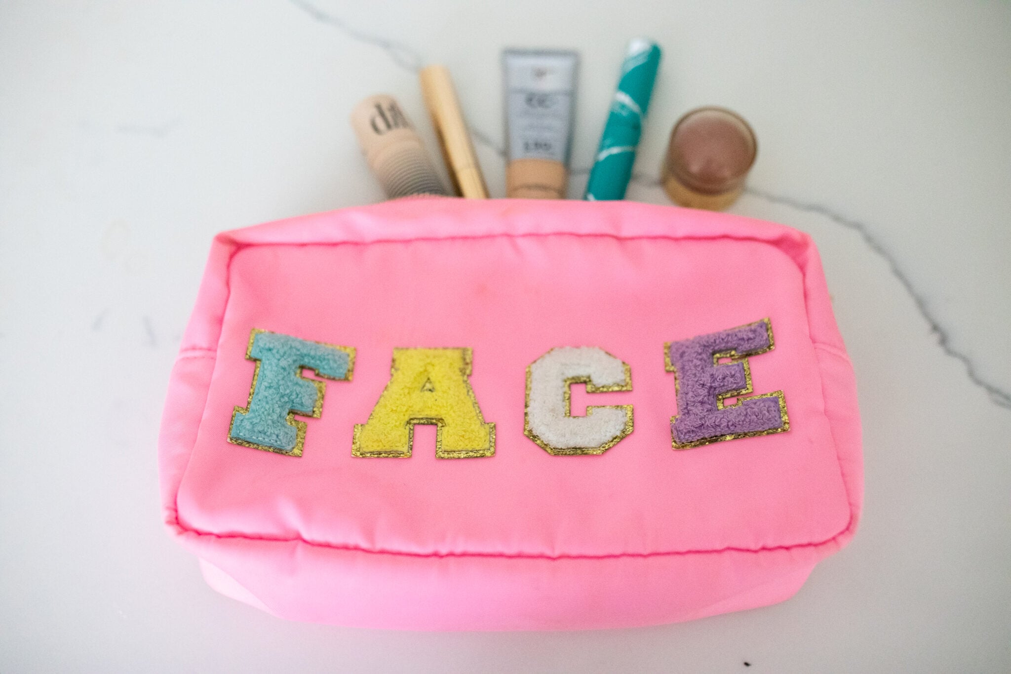 Pink makeup bag with colorful FACE lettering and beauty products inside