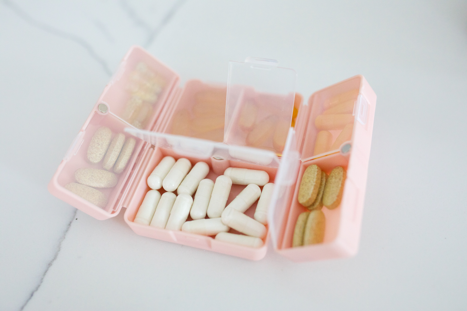 Pink travel pill organizer with compartments filled with vitamins and supplements