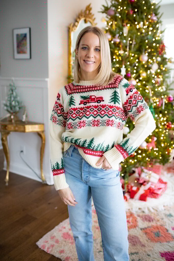 Christmas sweater in classic red, white, and green with a pickup truck carrying a tree